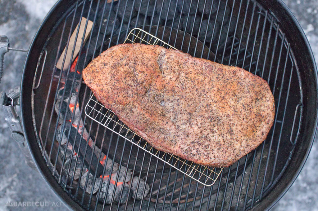 brisket placed in the middle of a charcoal grill surrounded by the charcoal snake