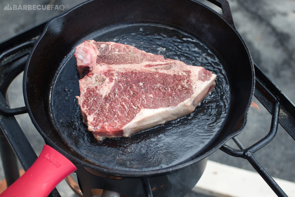 placing t-bone steak on cast iron skillet