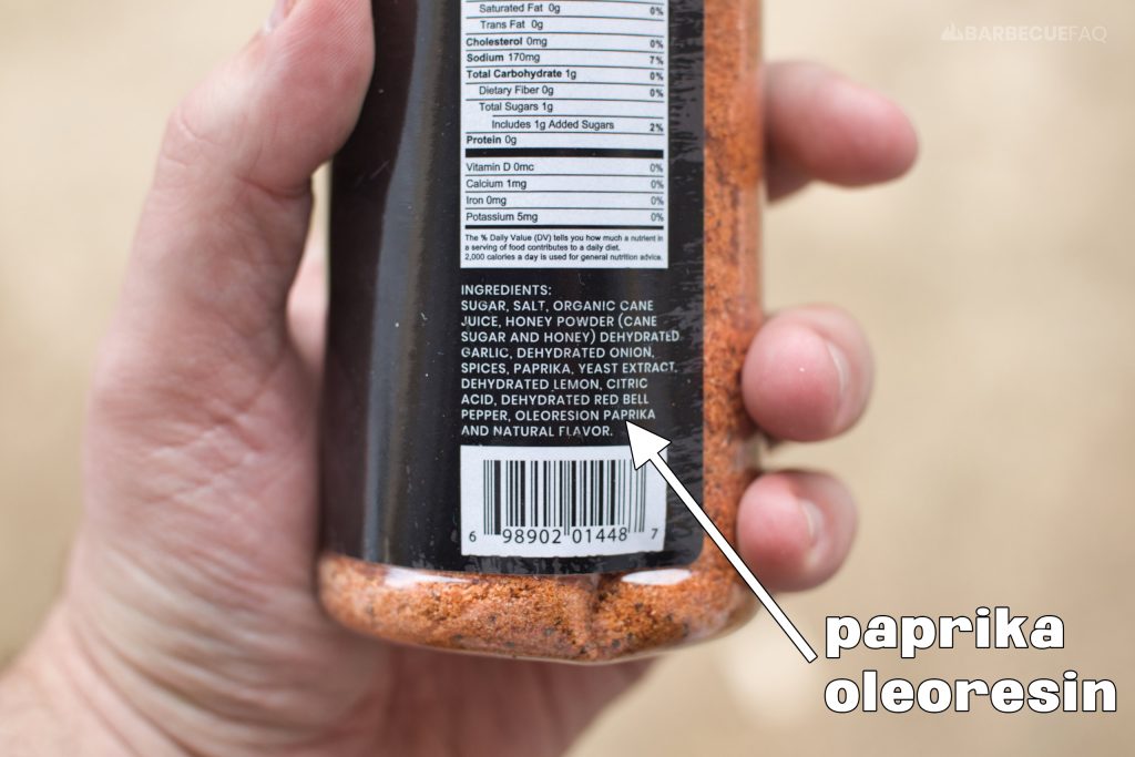 person holding a bbq rub shaker bottle with an arrow pointing to paprika oleoresin