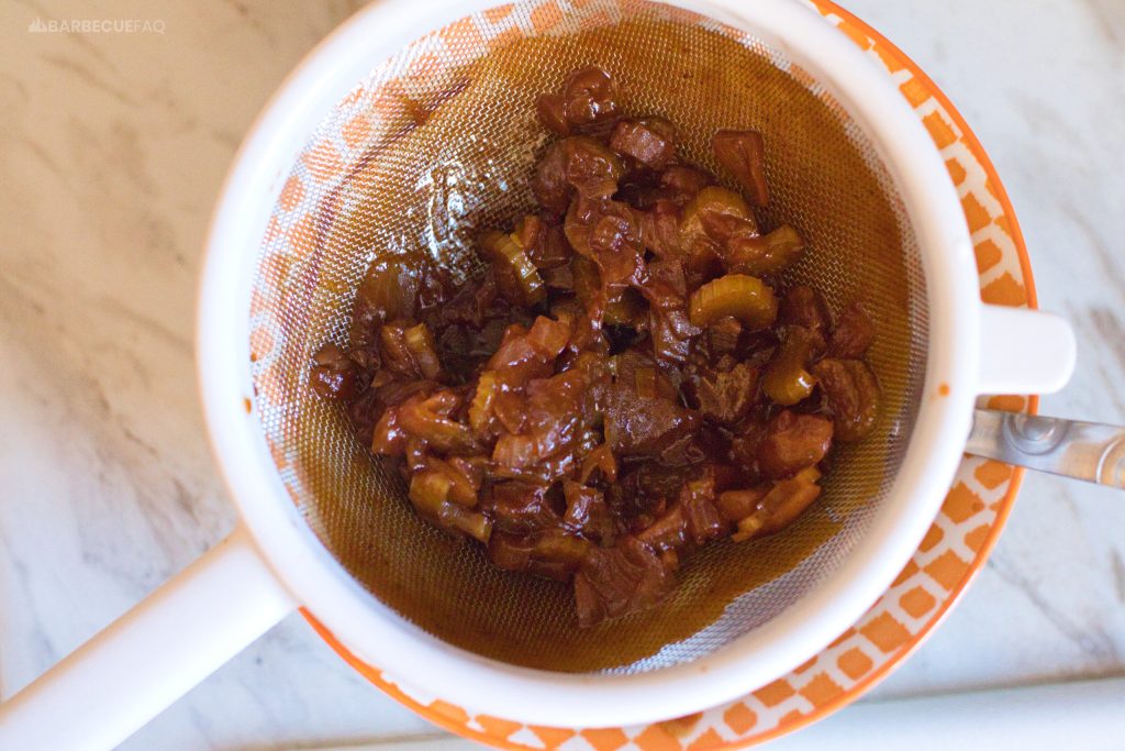 filtering onions and celery from bbq sauce with a mesh sieve